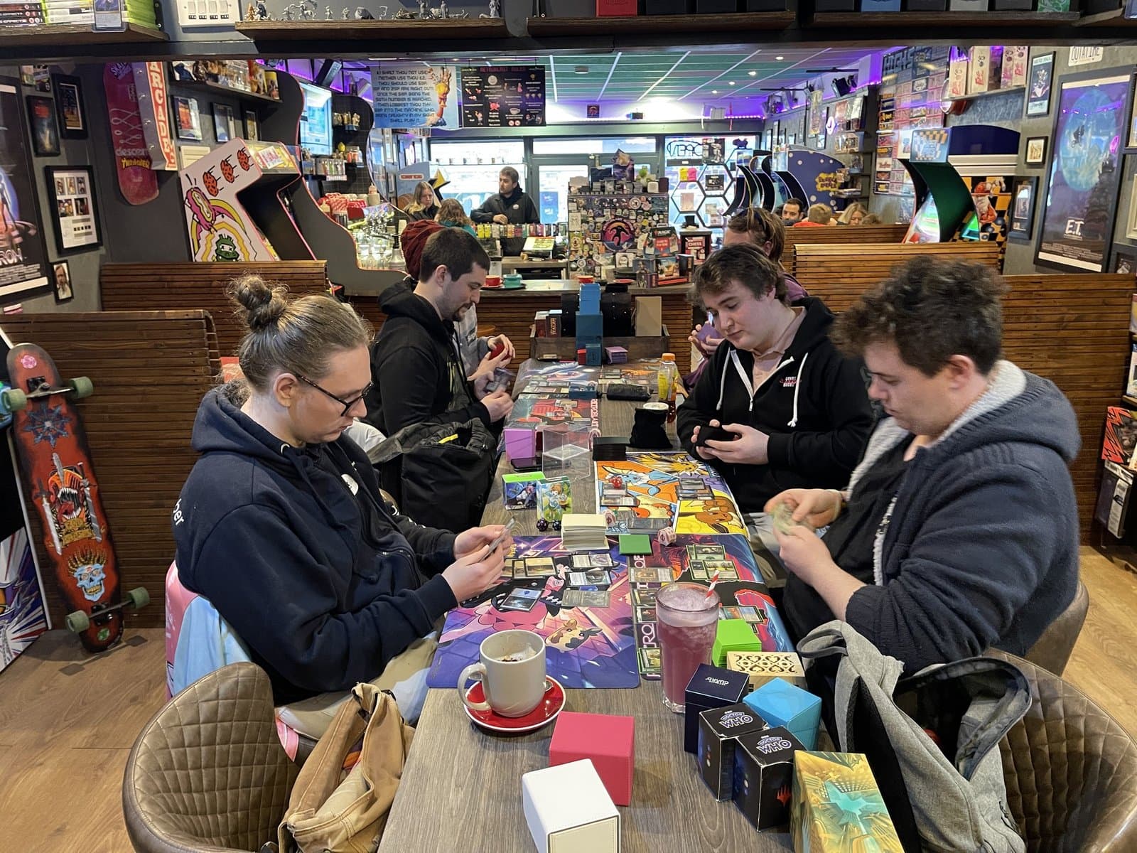 Tabletop night — four players mid-game with cards and boosters across the table