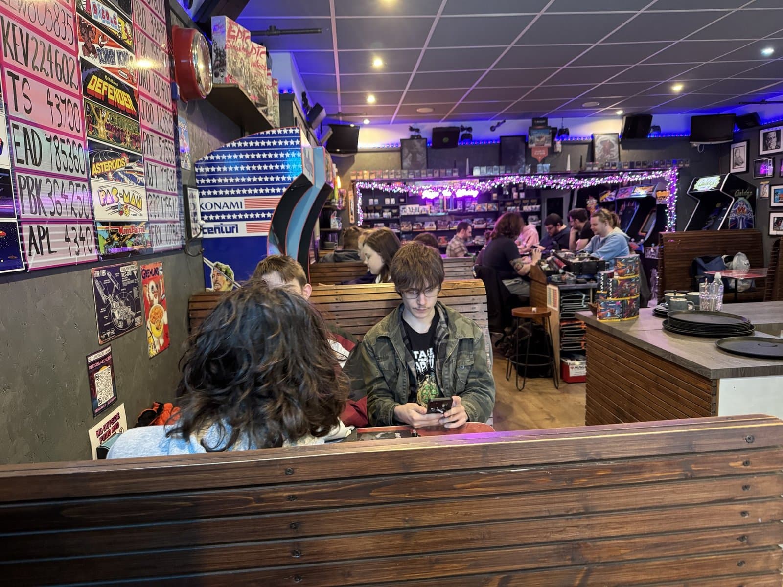 Booth seats at the bar — Konami badge, vintage number plates and regulars mid-game
