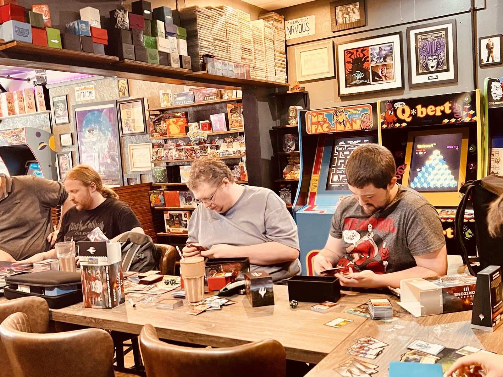 Board-game shelves and Q*bert and Ms Pac-Man cabinets behind a tabletop session