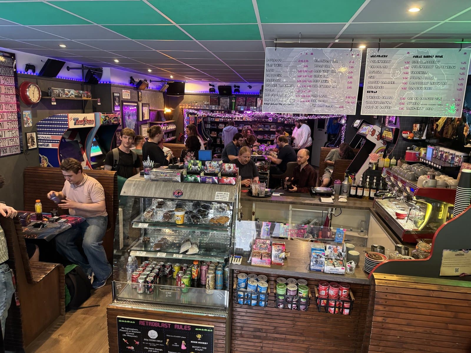 Kev and Beth behind the RetroBlast counter — coffee bar, arcade cabinets, regulars at the bar
